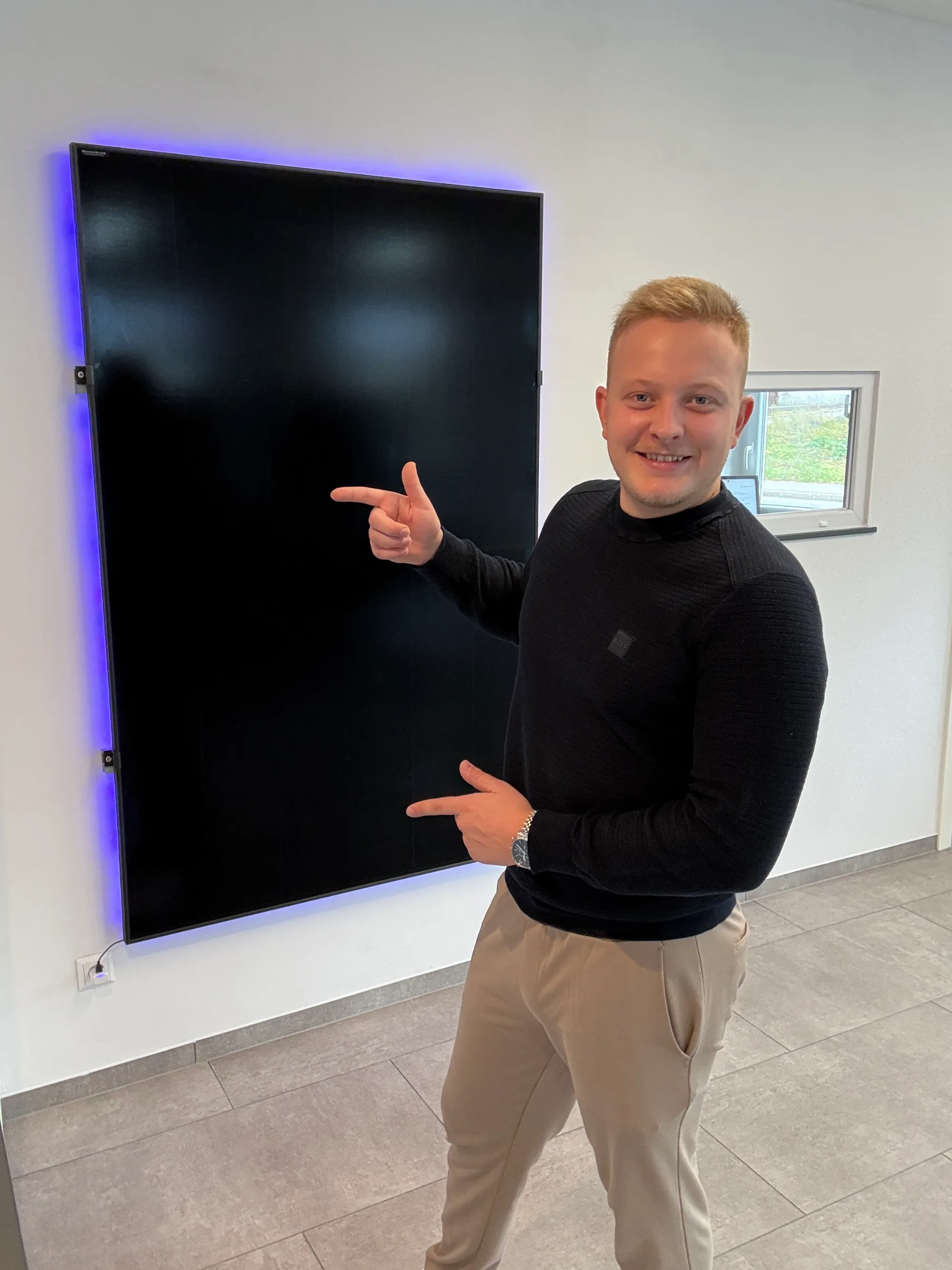 Samuel zeigt auf ein Full-Black Solarmodul im Showroom in Engstingen