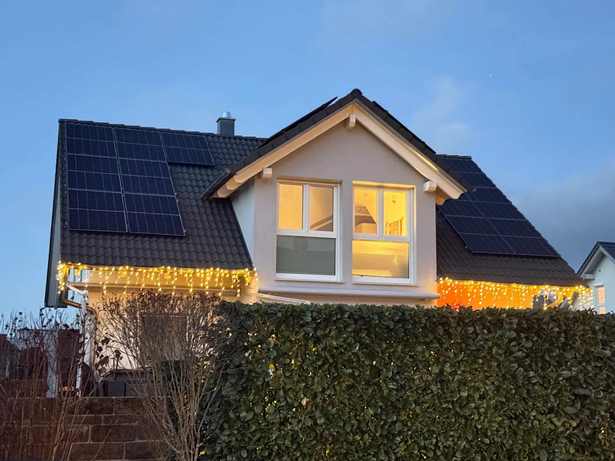 Einfamilienhaus mit Photovoltaikanlage am Abend, die Fenster sind beleuchtet