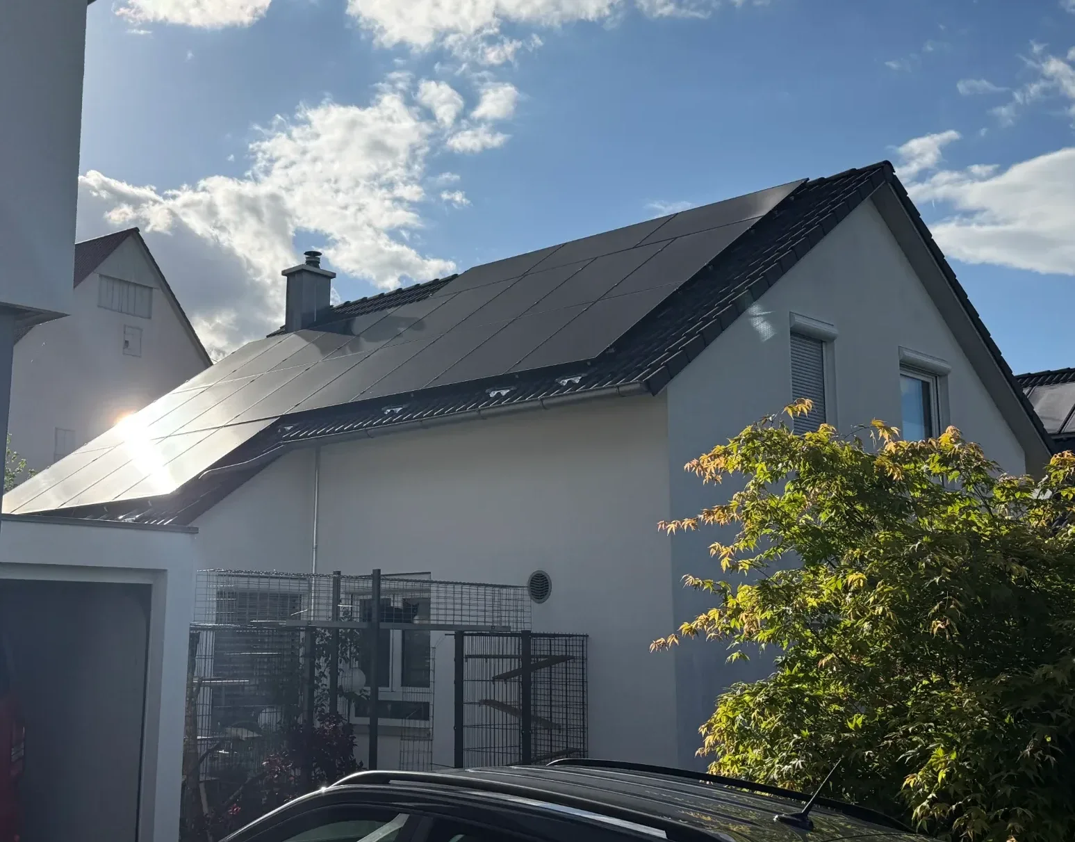 Photovoltaikanlage auf dem Satteldach eines weißen Einfamilienhauses bei Sonnenschein.