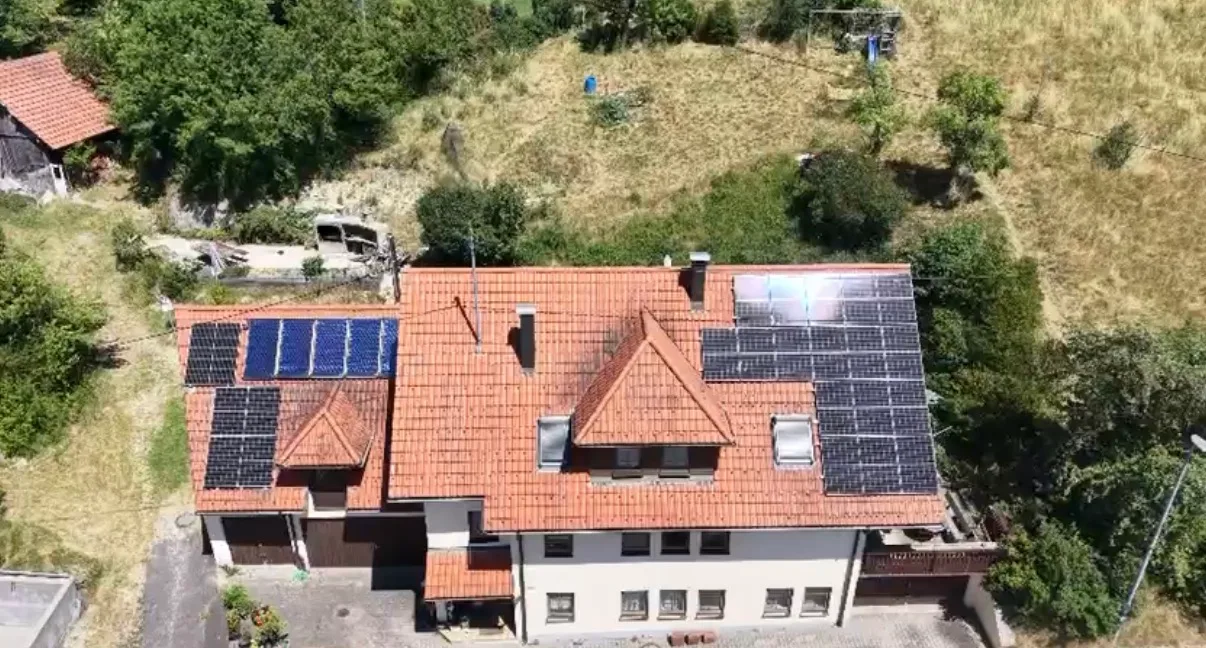 Luftaufnahme mehrerer Wohnhäuser in Hanglage, auf zwei Ziegeldächern liegen Photovoltaikmodule