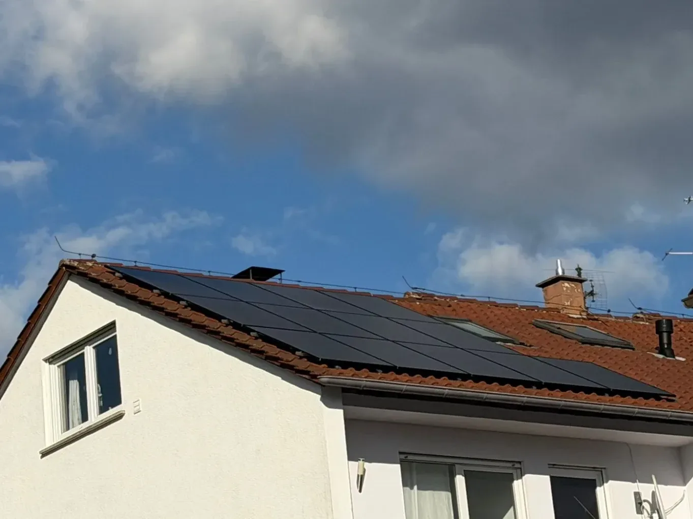 Photovoltaikanlage auf dem roten Ziegeldach eines Wohnhauses unter blauem Himmel.